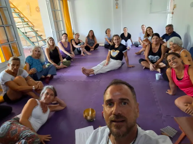 Un grupo de personas sentado en círculo sobre colchonetas violetas durante una práctica, en una sala con ventanales y luz natural. Marcelo Poppi en primer plano, junto a un cuenco tibetano.