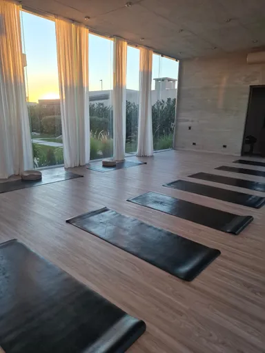 La sala vacía antes de empezar, con las colchonetas ya extendidas sobre el piso de madera y el sol bajando detrás de los ventanales.