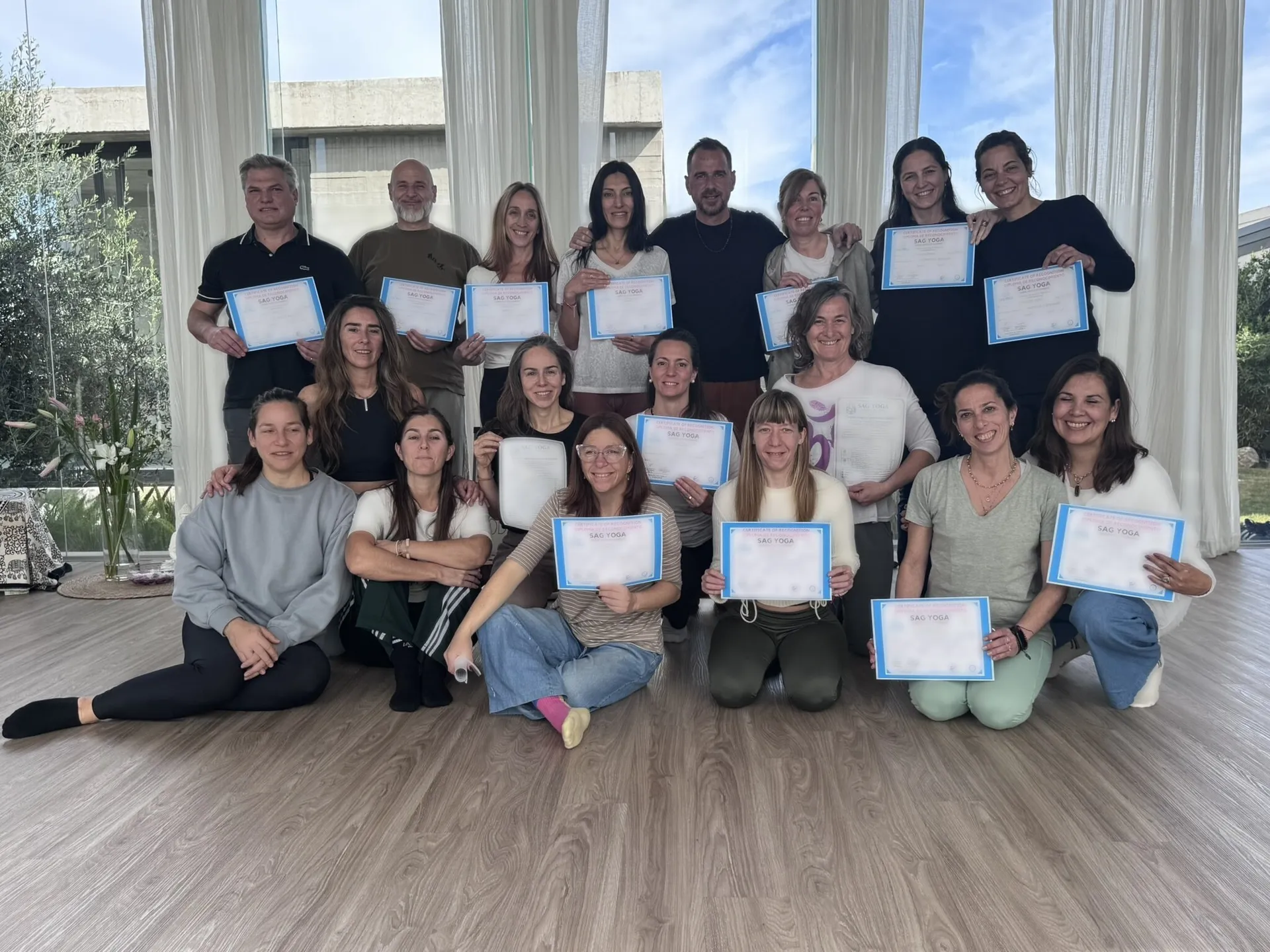 El grupo de egresadas y egresados del instructorado, en tres filas dentro de una sala con ventanales y cortinas claras, sosteniendo sus diplomas.