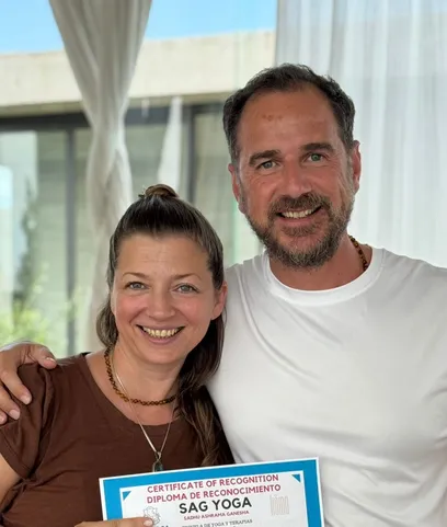 Marcelo Poppi junto a una egresada, los dos sonriendo a cámara, sosteniendo el diploma de instructora de meditación de SAG Yoga.